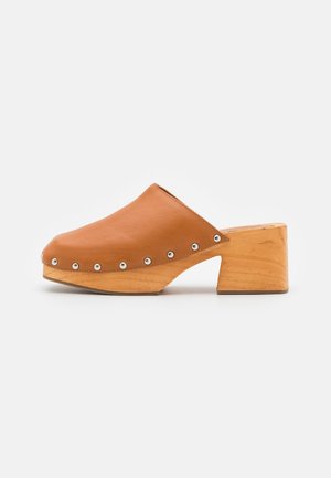 Sabot à enfiler en cuir fauve avec talon bloc en bois et détails en clous argentés le long du bord, présenté sur un fond blanc.