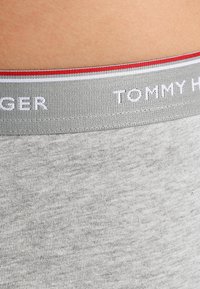 Grå bomullsboxershorts med myk tekstur, med et midjebånd merket "TOMMY HILFIGER" i hvitt, akkompagnert av røde og hvite striper.