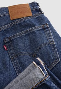 Μπλε τζιν Levi's από denim με πίσω τσέπη, καφέ δερμάτινη ετικέτα και διπλωμένο μπατζάκι με ορατή ραφή.