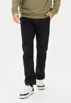 Black pants made of durable fabric with a straight leg design, featuring two side pockets and a smooth texture. Worn with white sneakers.