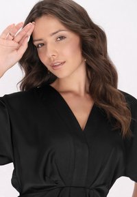 Rochie neagră, cu mâneci largi, de tip V, și textură moale; având o talie ajustată și detalii de design minimaliste.