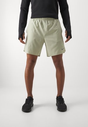 Nike Herren-Shorts in Hellgrün aus leichtem Material. Mit elastischem Bund und Seitenschlitzen für Bewegungsfreiheit. Kombiniert mit schwarzen Schuhen.