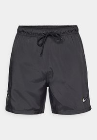 Svarte treningsshorts laget av lett, glinsende stoff; har elastisk liv med snor og en liten logo på kanten.
