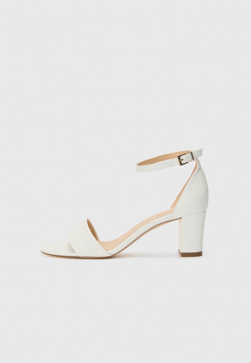Sandale à talons hauts blanche, ouverte sur le bout, avec une large sangle sur le pied, une sangle de cheville avec boucle et un talon épais. Texture lisse, design minimaliste.