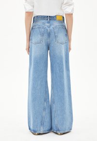 Helle blaue High-Waisted Jeans mit weitem Bein, haben eine ausgewaschene Textur, Gesäßtaschen und ein gelbes Markenschild am Bund.