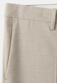 Pantaloni in tessuto beige con passante per cintura e piega laterale, che mostrano dettagli di trama e cuciture.