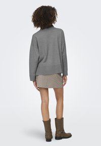 Suéter gris de gran tamaño con dobladillo acanalado, combinado con una minifalda de patrones y botas marrones altas hasta la rodilla con detalles de hebilla.