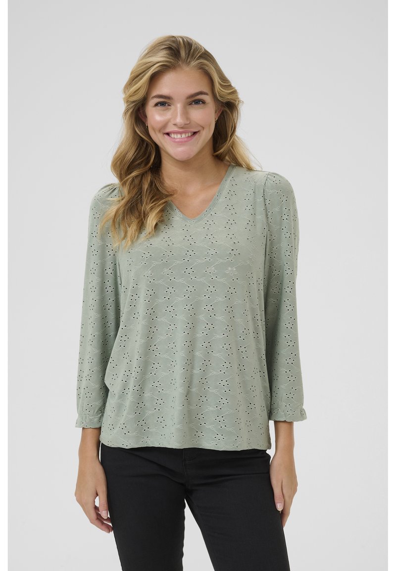 Haut vert clair en V avec un motif œillet décoratif et des manches trois-quarts. Tissu doux avec une coupe décontractée.