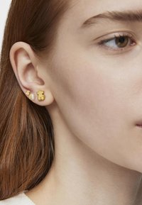 Złote kolczyki w kształcie misia i gwiazdy, o gładkiej fakturze, małych rozmiarach oraz delikatnych detalach na kształtach.