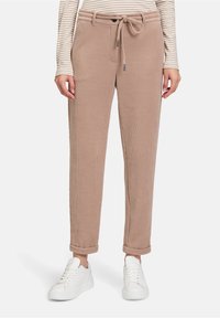 Beżowe dresowe spodnie z prążkowanym wzorem, z regulowanym ściągaczem w pasie, z mankietami na dole i bocznymi kieszeniami, zestawione z białymi sneakersami.