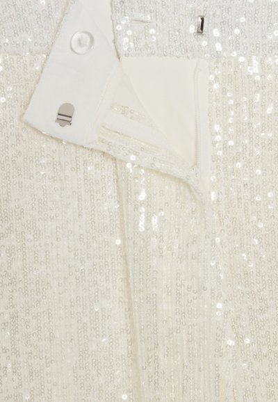 Indumento bianco con superficie di paillettes, dotato di chiusura con zip e dettaglio di bottone. L'interno è foderato con un tessuto liscio.