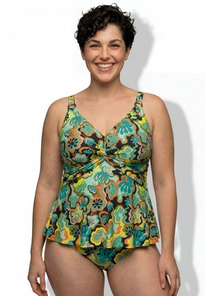 Uśmiechnięta kobieta o krótkich kręconych włosach nosi kolorowy tankini w kwiatowy wzór na białym tle.