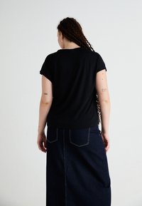 Μαύρη κοντομάνικη μπ�λούζα από υφαντό ύφασμα, σε συνδυασμό με μια σκούρα τζιν φούστα που διαθέτει πίσω τσέπες και εμφανή ραφή.