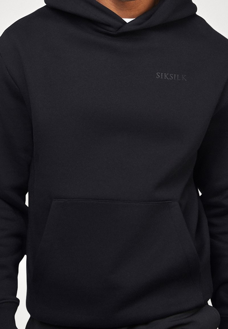 Hoodie noir en tissu doux, doté d'une poche kangourou et d'un logo discret sur la poitrine. Coupe standard avec un capuchon à cordons.