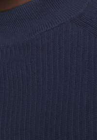 Zbliżenie na granatowy, prążkowany materiał dzianinowy z grubym, złożonym kołnierzem oraz teksturowanymi pionowymi liniami.