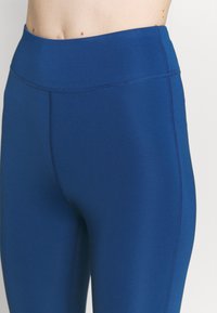 Niebieskie legginsy o wysokim stanie, wykonane z elastycznej tkaniny, z gładką teksturą i płaskimi szwami dla większego komfortu.