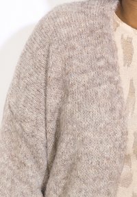 Gaišbeige adīts kardigans ar mīkstu, teksturētu audumu, ar atvērtu priekšpusi un brīvu piegriezumu. Akcenti ar rakstainu topu zem tā.