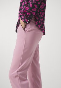 Fitted pink trousers made of a smooth fabric with side pockets, paired with a black blouse featuring multicolored lip print and cuff buttons.