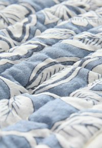 Tessuto trapuntato con un design floreale nei toni del blu e del bianco. La texture è morbida e il motivo include foglie e fiori contornati.
