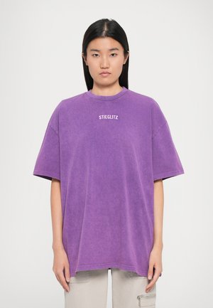 Camiseta oversized morada de un tejido suave y relajado. Cuenta con un escote tipo crew y un logo blanco "STIEGLITZ" centrado en el pecho.