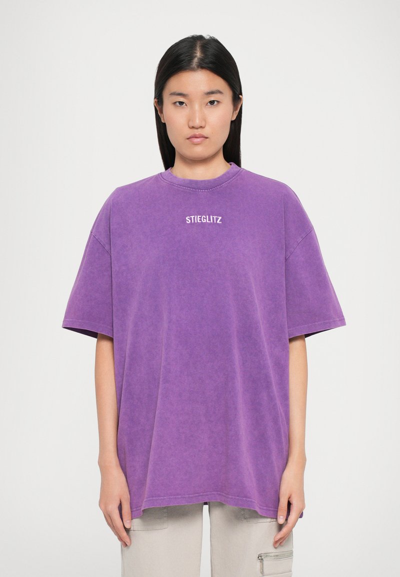 Lilla oversized t-skjorte i et mykt, avslappet stoff. Har en rund halslinning og en hvit "STIEGLITZ"-logo sentrert på brystet.