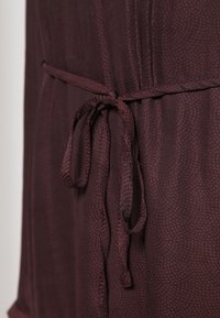 Zbliżenie na ciemnogranatową tkaninę zawiązaną w kokardę, z wąskim, strukturalnym paskiem wokół talii.