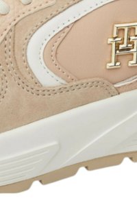 Sneaker in suede beige con dettagli bianchi, logo dorato e suola texturizzata. Forma arrotondata con cuciture decorative.