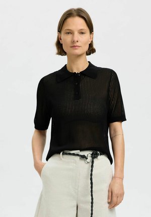 Polo shirt nera a maniche corte realizzata in tessuto trasparente e rigato, con colletto e tre bottoni. Abbinata a pantaloni chiari e di taglio morbido.