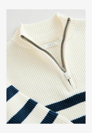 Suéter de punto acanalado color crema con cremallera de un cuarto y rayas en color navy, que presenta una cremallera plateada y una etiqueta que dice "NEXT". Textura suave, diseño de punto ajustado.