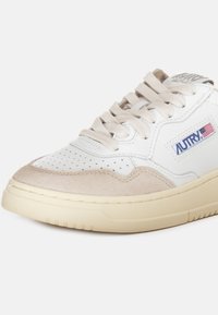 Sneaker in pelle bianca con accenti in suede beige, punta perforata, suola in gomma crema e logo brandizzato con un dettaglio a bandiera.