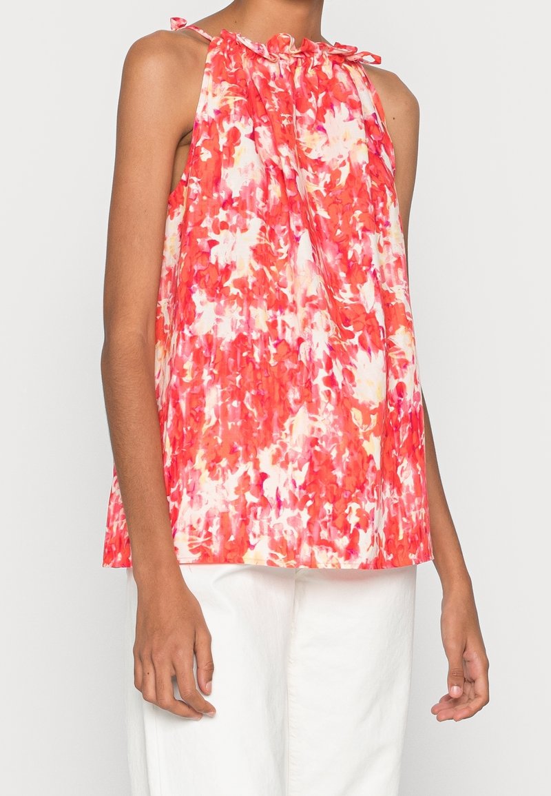 Haut à col licou floral en nuances de rose et blanc, avec un col à volants et des bretelles nouées, fabriqué en tissu léger.