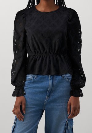 Zwarte blouse met lange pouf-mouwen, gestructureerde stof, elastische taille en sheer kantaccenten op de mouwen; gecombineerd met blauwe jeans.