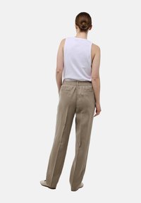 Pantalons en lin beige avec une coupe décontractée, présentant une jambe large, une taille élastique et deux poches arrière. Portés avec un débardeur blanc.