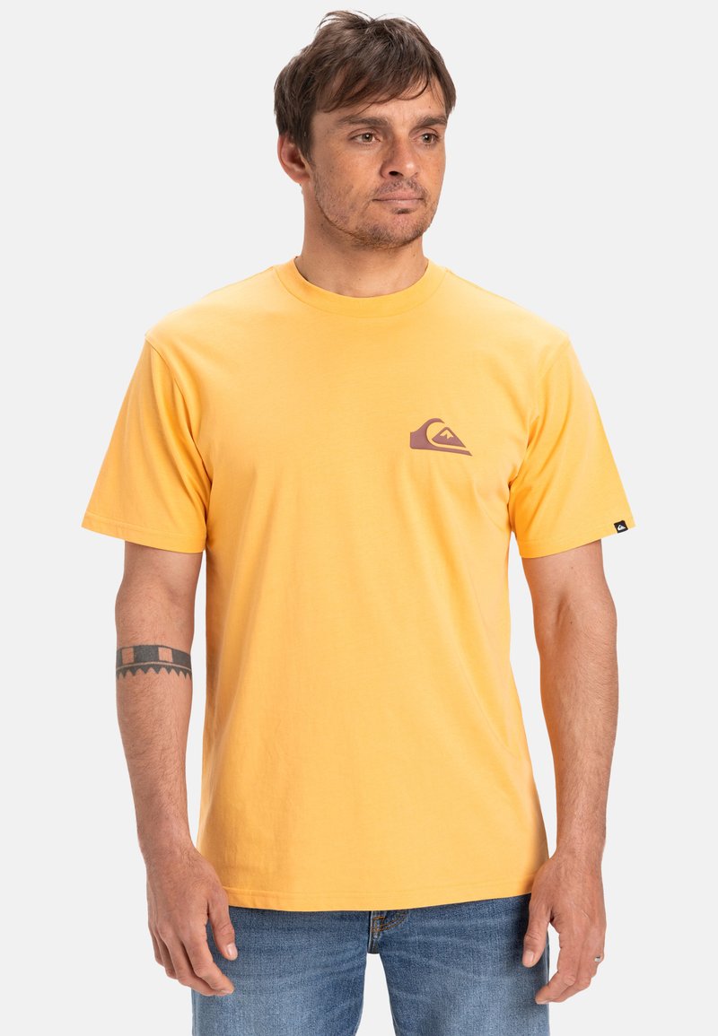 Camiseta de algodón amarilla con mangas cortas, cuello redondo y un pequeño logo morado en el pecho. Corte estándar sin patrones ni detalles.