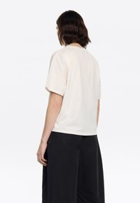 Crème kleurige t-shirt met korte mouwen, met een losse pasvorm en een ronde halslijn, gezien vanuit de achterkant. Soepele katoenstof, minimalistisch ontwerp.