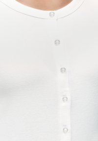 Gros plan sur le devant d'une chemise blanche à boutons avec six boutons transparents et un col rond sur une personne.