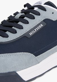 Zapatillas en navy y gris que presentan ante y tejido suave, con suela blanca y cordones negros. Logotipo de la marca visible en el lateral.