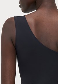 Černé plavky bez rukávů s hlubokým výstřihem, vyrobené z hladkého a elastického materiálu. Vyznačují se čistým, minimalistickým designem bez ozdob.