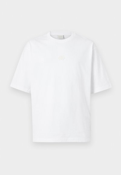 Λευκό βαμβακερό t-shirt με στρογγυλή λαιμόκοψη, κοντά μανίκια, με διακριτικό μπεζ λογότυπο λουλουδιού στο στήθος και άνετη εφαρμογή.