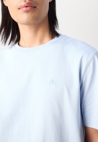 Light blue cotton t-shirt with a crew neckline and short sleeves. Features a small embroidered design on the left chest.