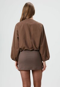 Bruine, lichte blouse met opgeblazen mouwen, gecombineerd met een strakke bruine mini-rok. Gladde stoftextuur, minimalistisch ontwerp.
