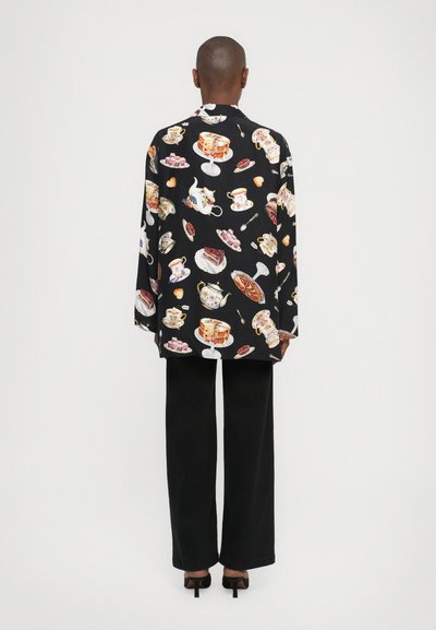 Black shirt featuring a colorful dessert and tea set print. The shirt has long sleeves and is paired with wide-leg black pants and heels.