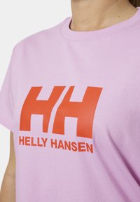 Světle růžové bavlněné tričko s velkým červeným logem "HH" a textem "HELLY HANSEN". Standardní kulatý výstřih a krátké rukávy. Hladká textura.