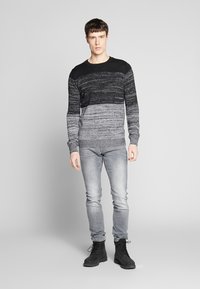 Čierny a šedý pruhovaný pletený sveter s okrúhlym výstrihom, skombinovaný so svetlosivými džínsami a čiernymi šnurovacími topánkami. Textúrovaný vzor po celom povrchu.