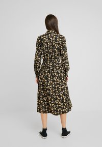 Mustapuku, jossa on keltainen ja valkoinen kukkakuosi, pitkät hihat, vyötäröllä vyö ja midi-pituus. Yhdistetty mustiin korkean varren lenkkareihin.