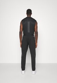 Svart sportig outfit med ärmlös topp och tapered byxor med reflexlinor. Materialet verkar lätt och har en slät yta.