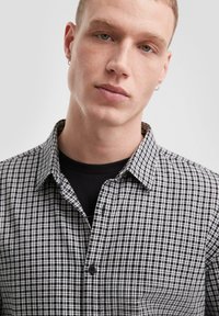 Zwart-wit geruite overhemd met een button-down kraag, gestructureerde stof en een zwarte binnenlaag zichtbaar bij de hals.