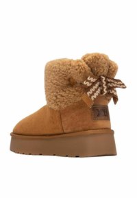 Stivaletto in suede marrone con un morbido interno in lana, una spessa suola platform e un fiocco decorativo marrone di lato. Logo Xti sul tallone.