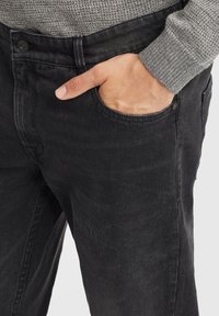 Jeans de mezclilla negra con un corte relajado, que cuentan con un detalle de bolsillo frontal y una textura sutil. La cinturilla incluye un cierre con botón.