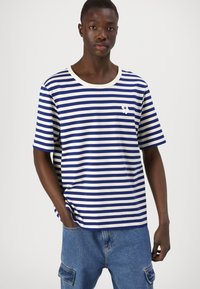 Camiseta a rayas en azul y blanco, de manga corta, con cuello redondo, que presenta un pequeño detalle gráfico en el pecho y un corte holgado.